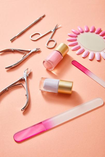 High angle view of bottles and samples of nail polish with manicure instruments on coral background - 写真・画像