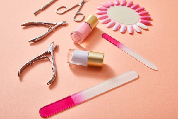 High angle view of bottles and samples of nail polish with manicure instruments on coral - Photo, Image