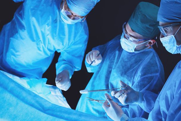 Grupo de cirujanos trabajando en quirófano tonificado en azul. Equipo médico realizando la operación - Foto, Imagen