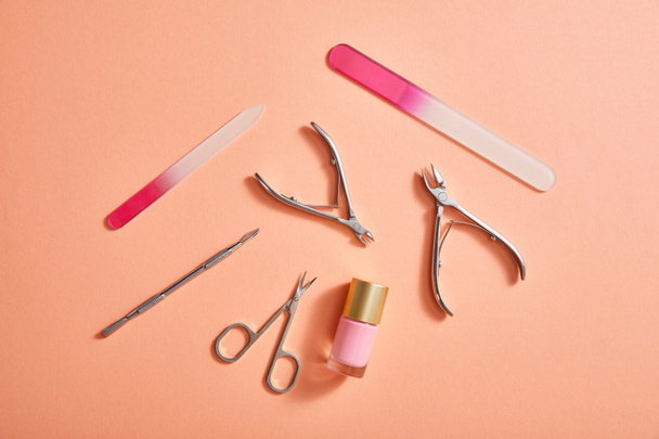 Top view of manicure instruments and bottle of pink nail polish on coral background - Photo, Image
