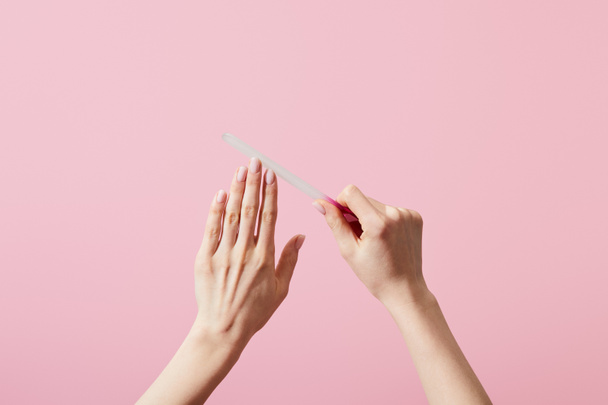 Cropped view of woman filing fingernails with nail file isolated on pink - Foto, Imagen