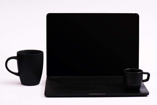 κούπες καφέ και μαύρο φορητό υπολογιστή με λευκή οθόνη σε λευκό  - Φωτογραφία, εικόνα