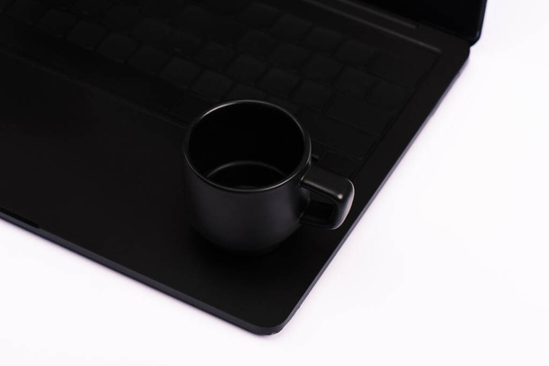 白に隔離された黒いノートパソコンのキーボードで飲むカップ  - 写真・画像