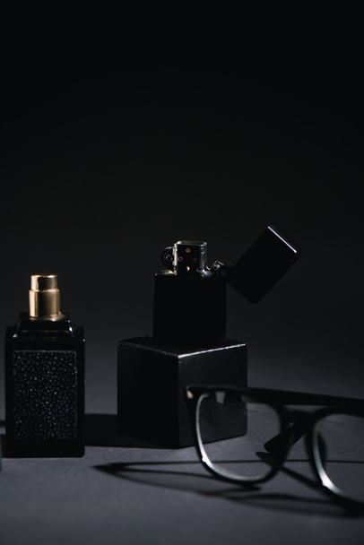 επιλεκτική εστίαση του αναπτήρα κοντά γυαλιά και μπουκάλι άρωμα σε μαύρο  - Φωτογραφία, εικόνα