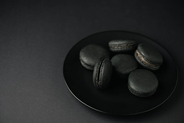 plate with tasty and dark macarons isolated on black  - Valokuva, kuva