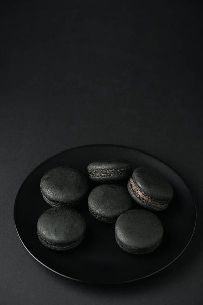 top view of plate with dark and tasty macarons on black  - Fotó, kép