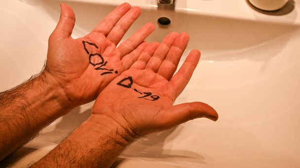 Koronavirus. Koncepční obraz nebezpečí viru: nápis na dlaních bělocha vyzdvihuje, jak napadá člověka. V pozadí umyvadlo na mytí a čištění. - Fotografie, Obrázek