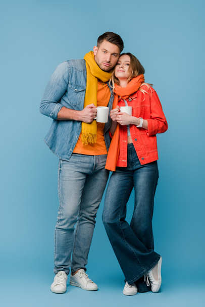couple malade en écharpes tenant des tasses avec des boissons chaudes sur bleu
 - Photo, image