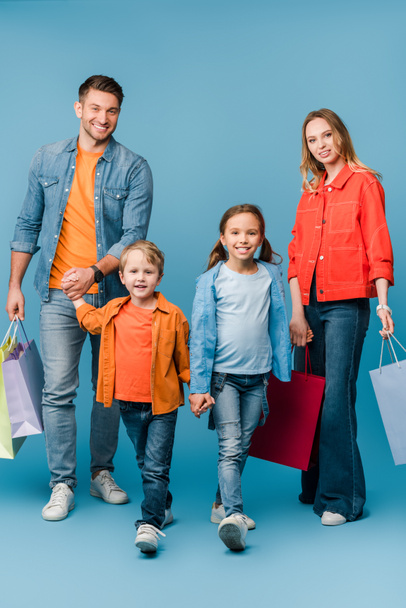 happy parents holding hands with children while holding shopping bags on blue  - Foto, imagen