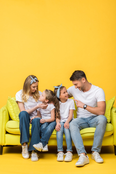 padres felices hablando con adorable hija e hijo mientras están sentados juntos en el sofá en amarillo
 - Foto, Imagen
