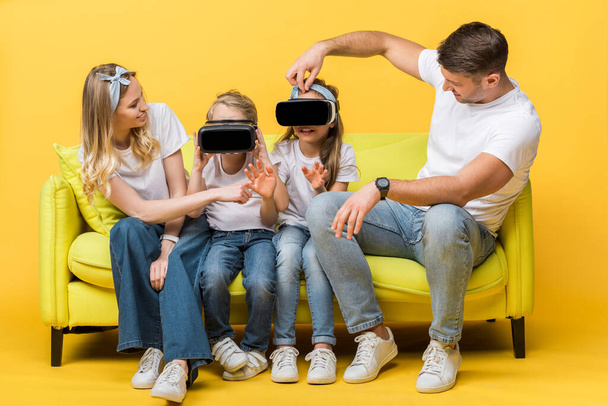 padres felices con hija e hijo en auriculares de realidad virtual sentados en el sofá en amarillo
   - Foto, imagen