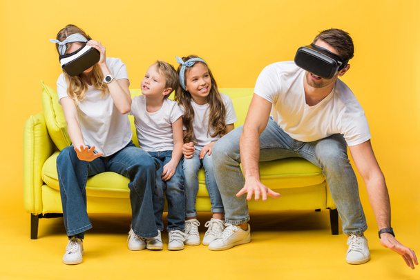 śmiejące się dzieci siedzące na kanapie z rodzicami w wirtualnej rzeczywistości zestawy słuchawkowe na żółto   - Zdjęcie, obraz
