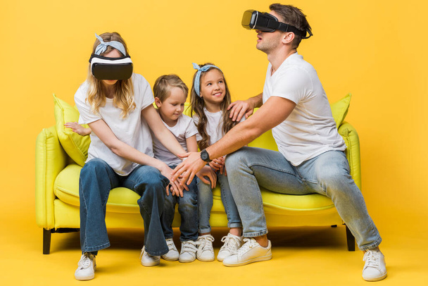 happy children sitting on sofa with parents in virtual reality headsets on yellow   - Fotó, kép