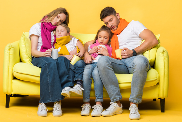 сонная семья с гриппом с закрытыми глазами, сидя на диване на желтом
   - Фото, изображение