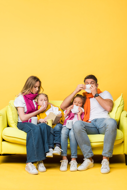sick family with napkins having runny noses while sitting on sofa on yellow - Fotoğraf, Görsel
