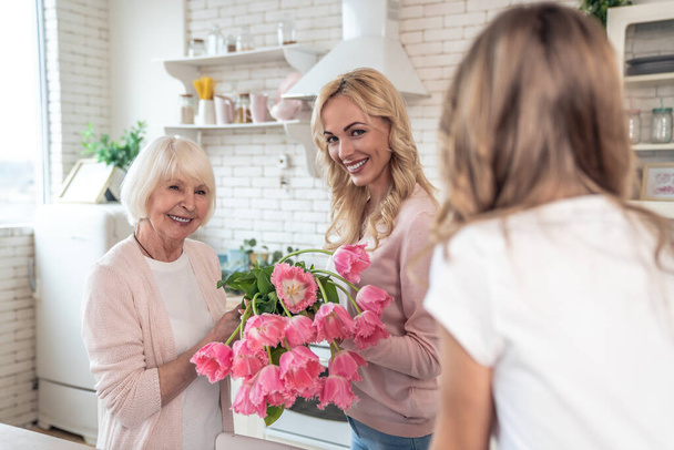 Senior woman and her attractive daughter spending time together at home. Cooking together on kitchen. Happy Mothers Day. Daughter presenting flowers to her mom. - Fotó, kép