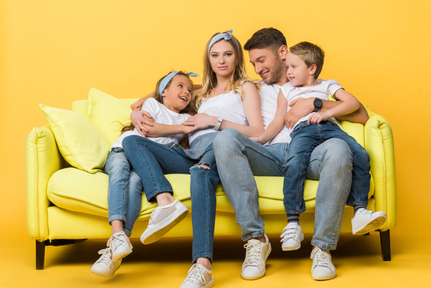Mère, père et enfants souriants et enceintes assis sur le canapé jaune
   - Photo, image