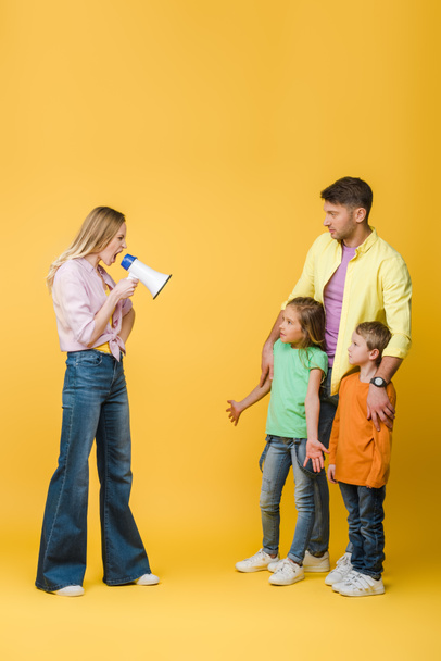 angry mother yelling into megaphone on confused kids and husband on yellow  - Foto, Imagem
