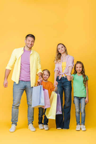 pais alegres de mãos dadas com crianças enquanto segurando sacos de compras no amarelo
  - Foto, Imagem