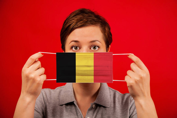 Coronavirus COVID-19 in Belgium. Woman in medical protective mask with the image of the flag of Belgium. The concept of preventing the spread of the epidemic and treating coronavirus. - Photo, image