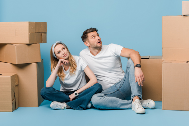 dreamy couple sitting with cardboard boxes for relocation on blue - Photo, Image