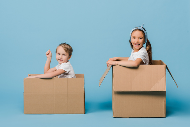 adorables hermanos alegres jugando en cajas de cartón en azul
 - Foto, Imagen