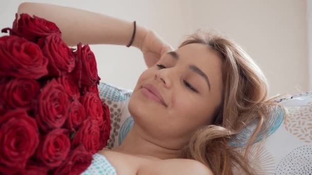 Beautiful young woman in bed with rose boquet. Smiling and dreaming. Sunny and bright day in the morning. Romantic concept. - Πλάνα, βίντεο