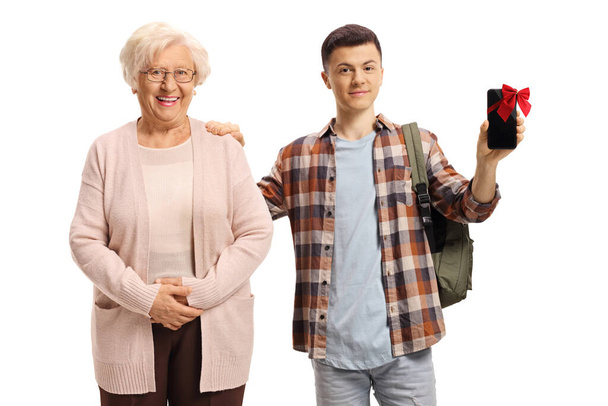 Teenageralter Student mit einem Mobiltelefon mit roter Schleife und einer älteren Frau, die isoliert auf weißem Hintergrund lächelt - Foto, Bild