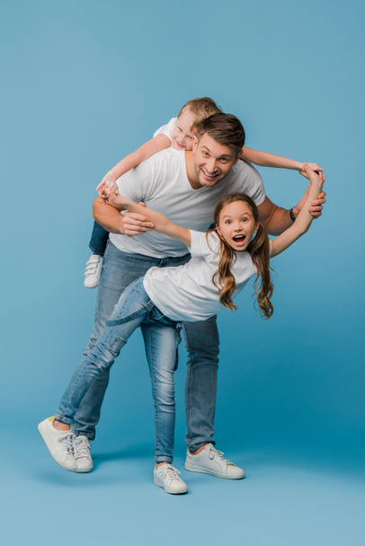 smiling father piggybacking and plating with kids on blue  - Valokuva, kuva