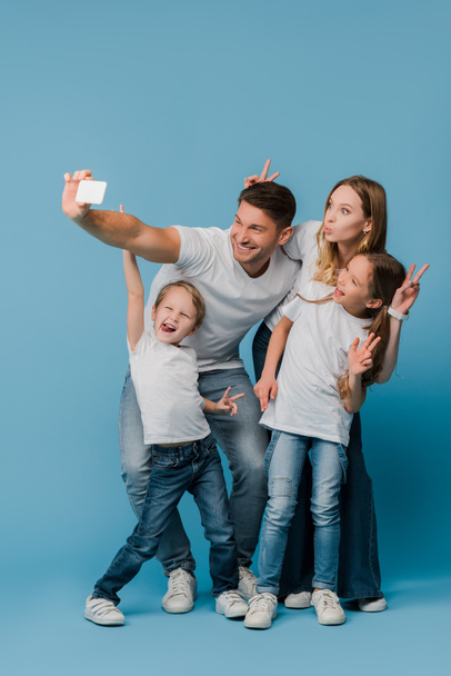 famille joyeuse montrant des signes de victoire tout en prenant selfie sur smartphone sur bleu
 - Photo, image