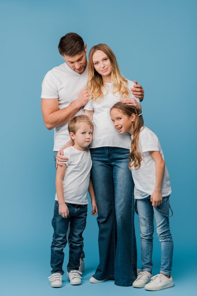 συναισθηματικός σύζυγος και παιδιά αγκαλιάζουν έγκυο γυναίκα στο μπλε  - Φωτογραφία, εικόνα