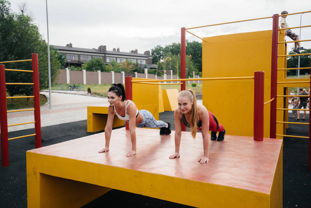 Athletic, sexy girls do push-UPS outdoors synchronously. Fitness, healthy lifestyle - Fotó, kép