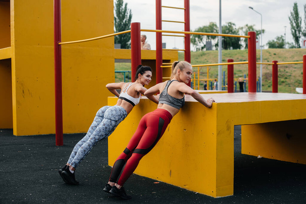 Athletic, sexy girls do push-UPS outdoors synchronously. Fitness, healthy lifestyle - Zdjęcie, obraz