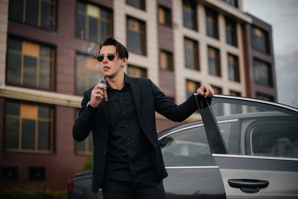 A stylish businessman smokes cigars near a luxury car. Fashion and business - Zdjęcie, obraz
