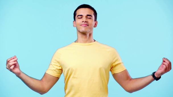 sonriente hombre de pie en meditación yoga pose con los ojos cerrados aislados en azul
 - Imágenes, Vídeo