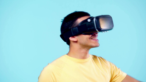 excited man gesturing while using vr headset isolated on blue - Materiał filmowy, wideo