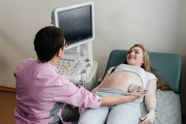 A pregnant girl gets an ultrasound of her abdomen at the clinic. Medical examination - Фото, изображение