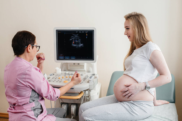 Lääkäri neuvoo raskaana olevaa tyttöä klinikan ultraäänen jälkeen. Lääkärintarkastus - Valokuva, kuva