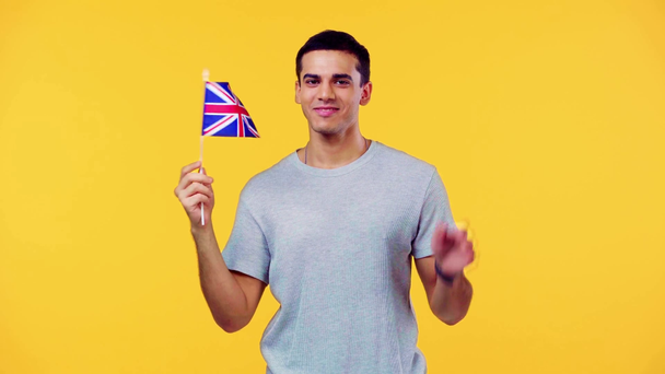 šťastný muž s malou vlajkou Velké Británie ukazuje ahoj izolované na žluté - Záběry, video