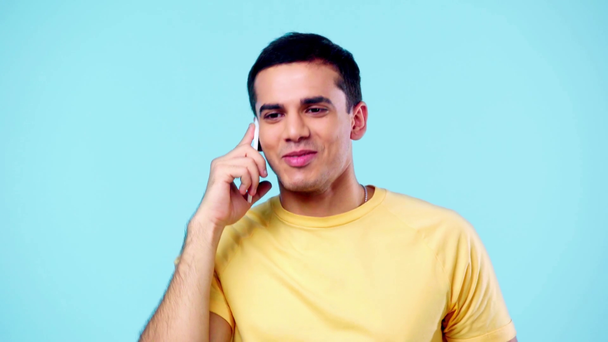 handsome young man smiling while talking on smartphone isolated on blue - Footage, Video