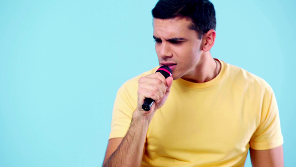 vzrušený mladý muž zpívající s mikrofonem izolované na modré - Záběry, video