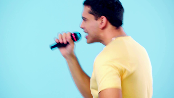 widok z boku podekscytowany człowiek z mikrofonu taniec i śpiew odizolowany na niebiesko - Materiał filmowy, wideo