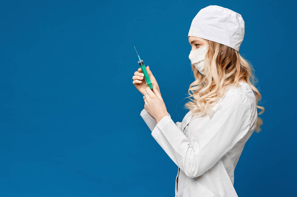 Beautiful young nurse in medical robe holding syringe, isolated over blue background with copy space. Medical injection. Pretty young woman doctor with a syringe. Pharmacy and medicine concept - Zdjęcie, obraz