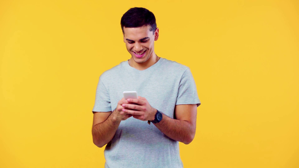 uśmiechnięty mężczyzna czatujący na smartfonie odizolowanym na żółto - Materiał filmowy, wideo