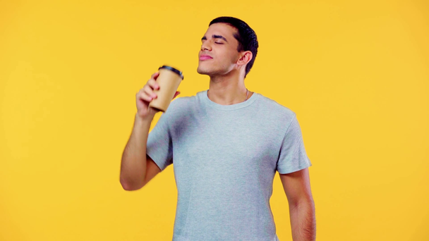 pleased man smiling while drinking coffee to go isolated on yellow - Footage, Video