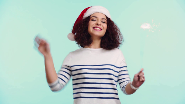 alegre chica en santa hat celebración sparkler y agitando mano aislado en turquesa
 - Imágenes, Vídeo