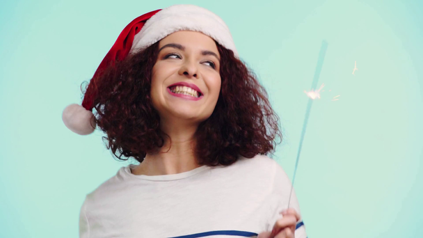 happy curly girl in santa hat holding bengal light isolated on turquoise - Video