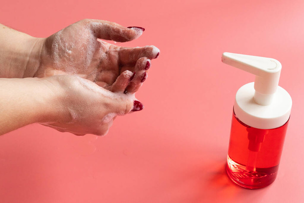 Femme savonne les mains avec du savon liquide sur fond rose
 - Photo, image