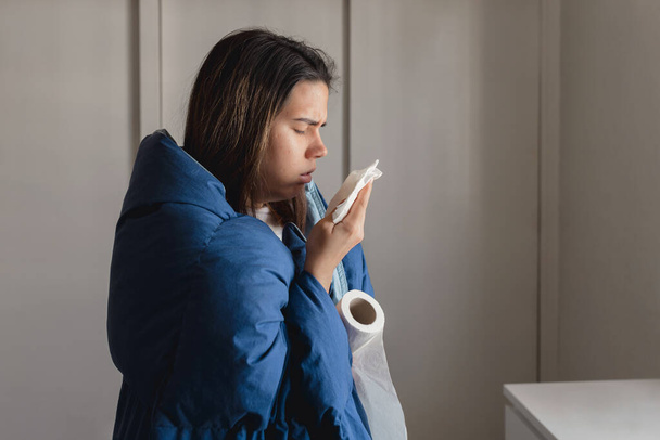 Mladá nemocná žena infikovaná koronavirem kašle do tkáně, zatímco je přikrytá modrou dekou v bezpečí svého domova. Celosvětová virová choroba ve Španělsku. - Fotografie, Obrázek