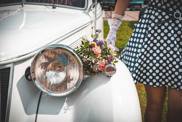 Beyaz retro araba, 1950 'lerin tarzında bir kızın yanında, bir buket kır çiçeği.. - Fotoğraf, Görsel